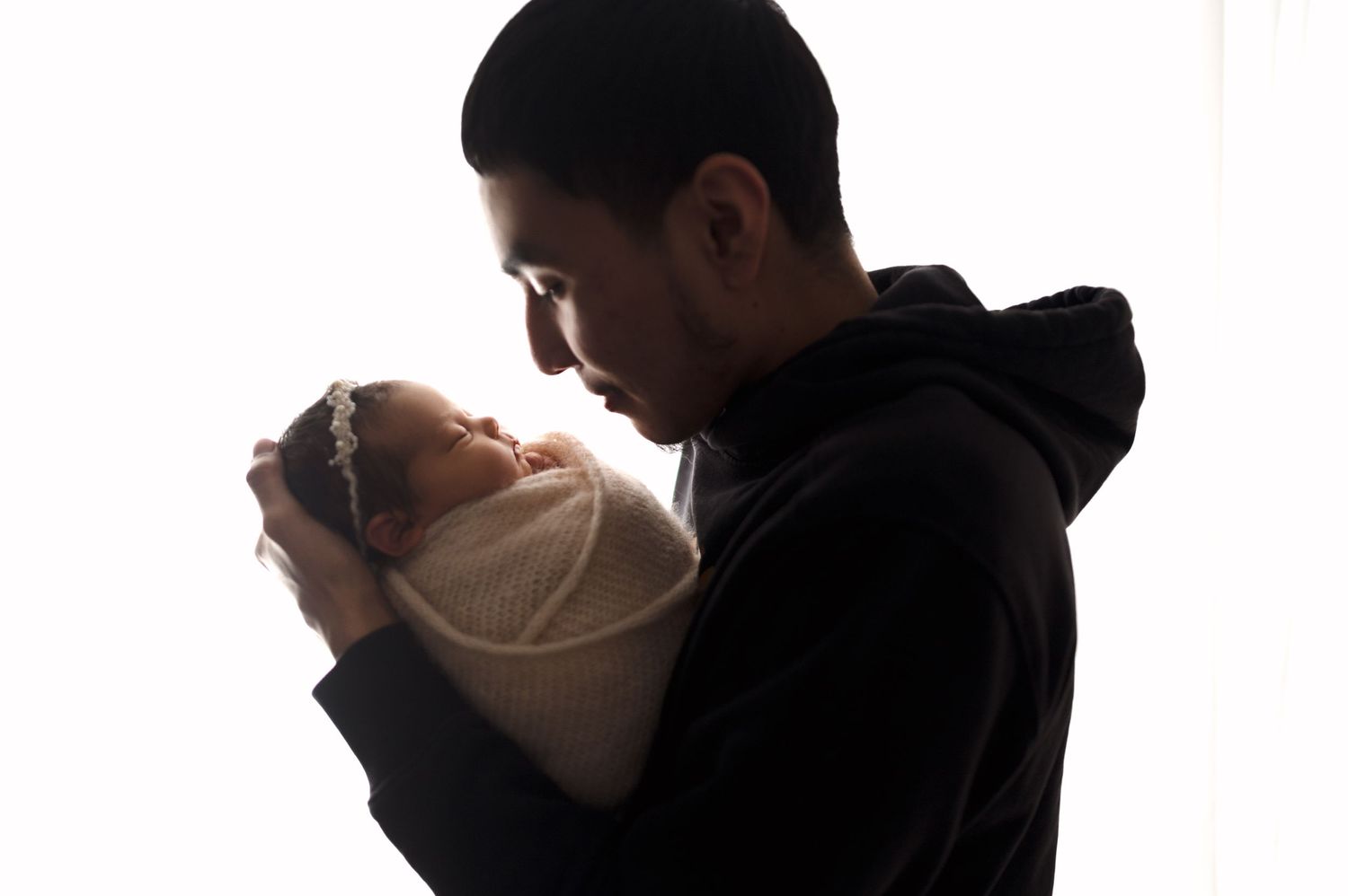 Side profile silhouette of parents bonding with newborn against bright backdrop.
