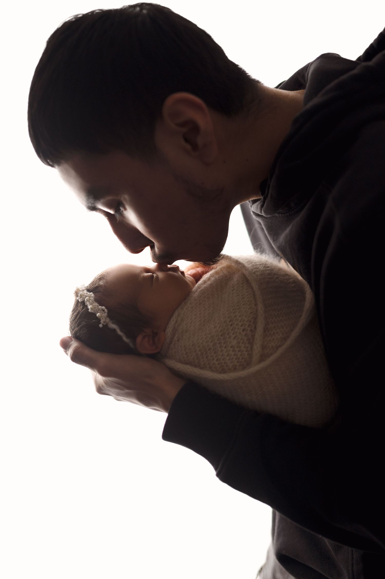 Close up silhouette of parents gently cradling newborn in white room.