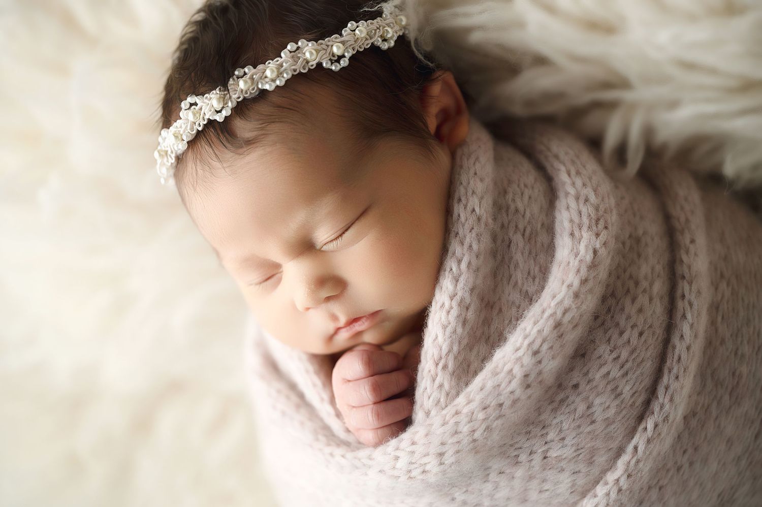 Sleeping newborn posed with cream textured linens and delicate lace accessories in soft natural lighting.