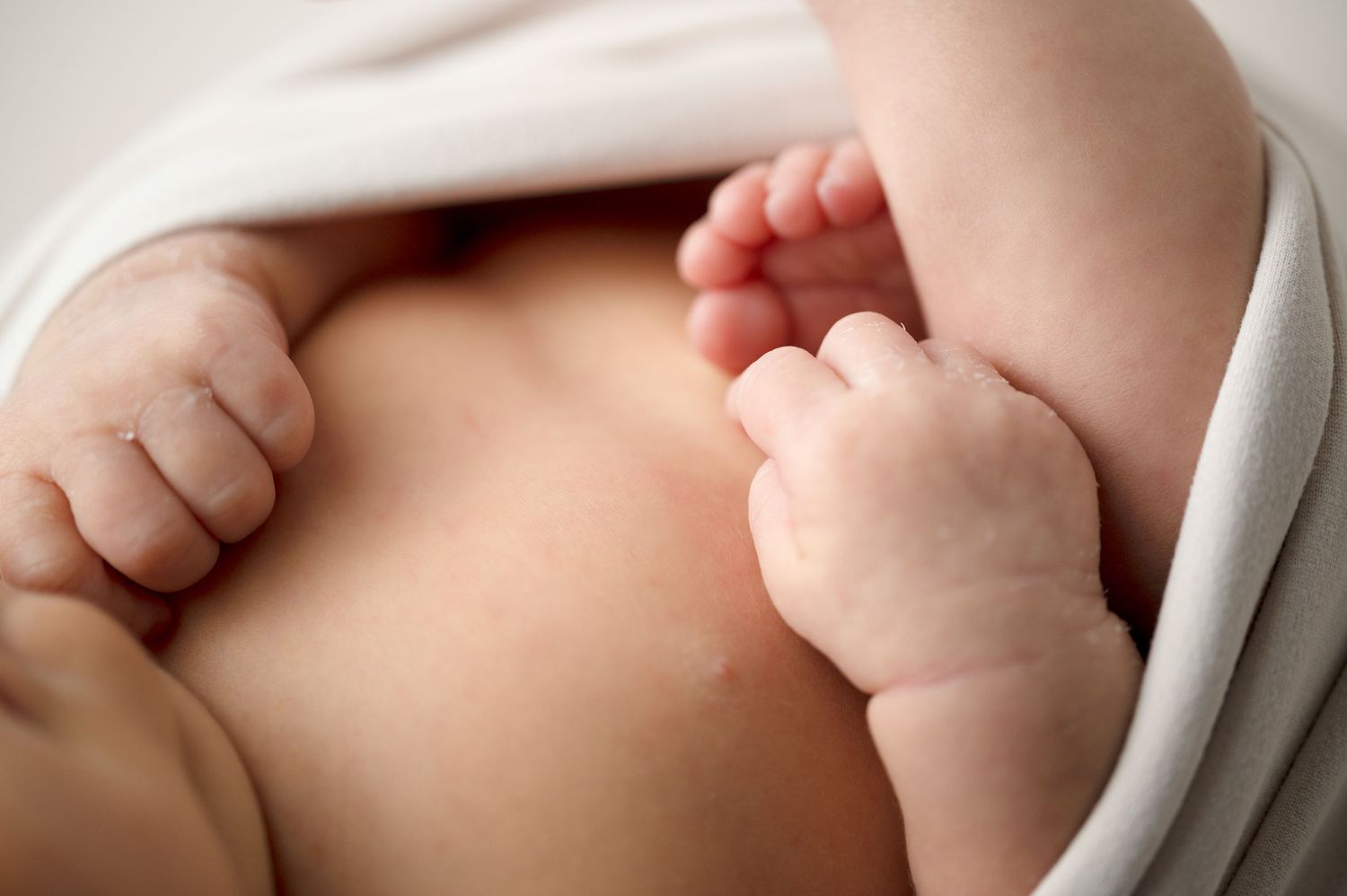 Close-up detail of tiny newborn baby feet and hands wrapped in soft white fabric.