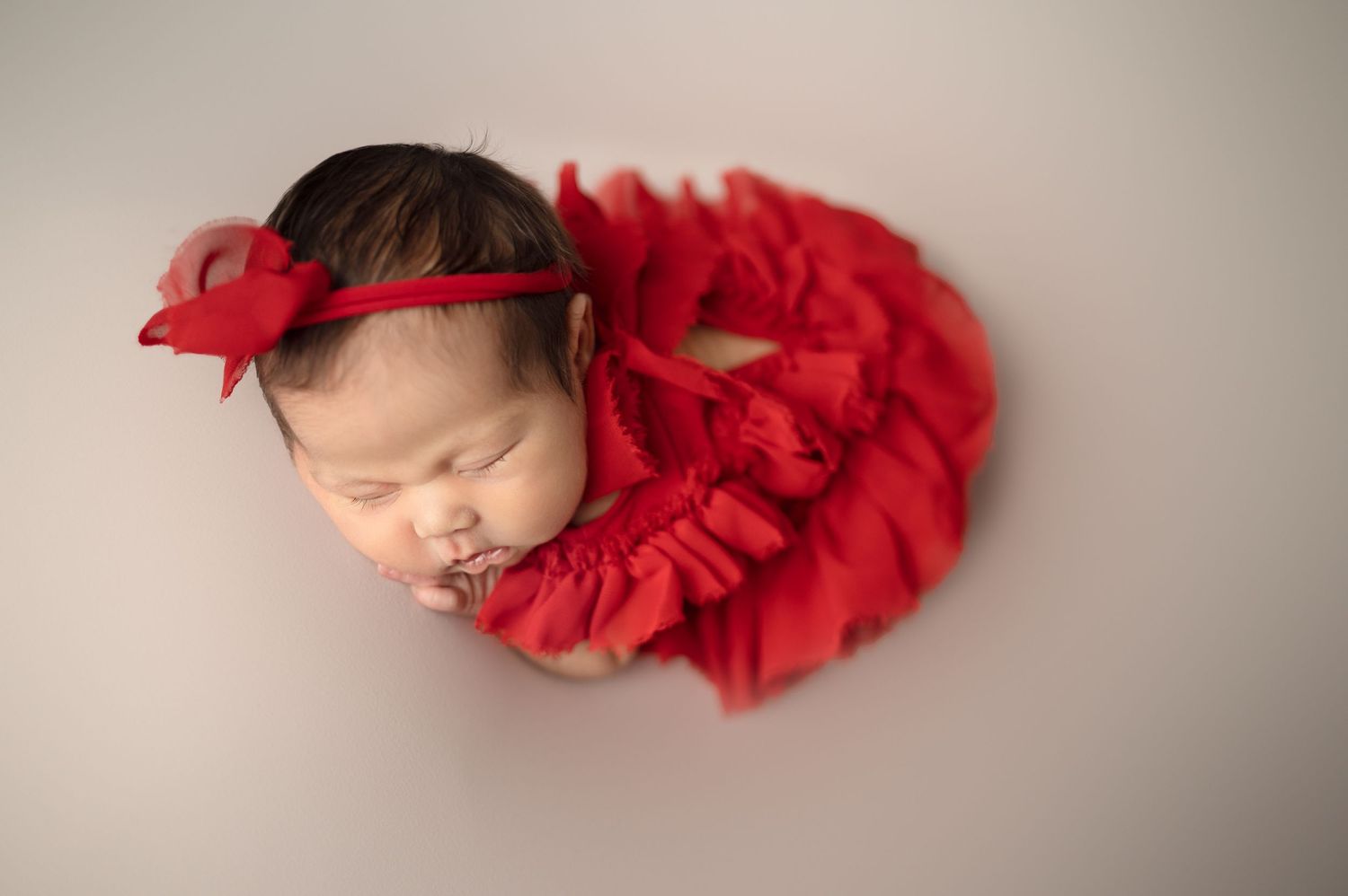 Newborn posed with vibrant red tulle wrap on neutral gray backdrop.