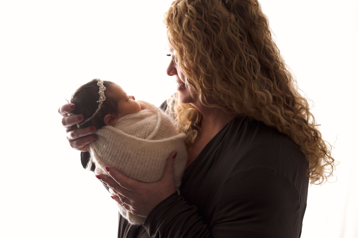 Parents in dark clothing sharing tender moment with baby against white background.