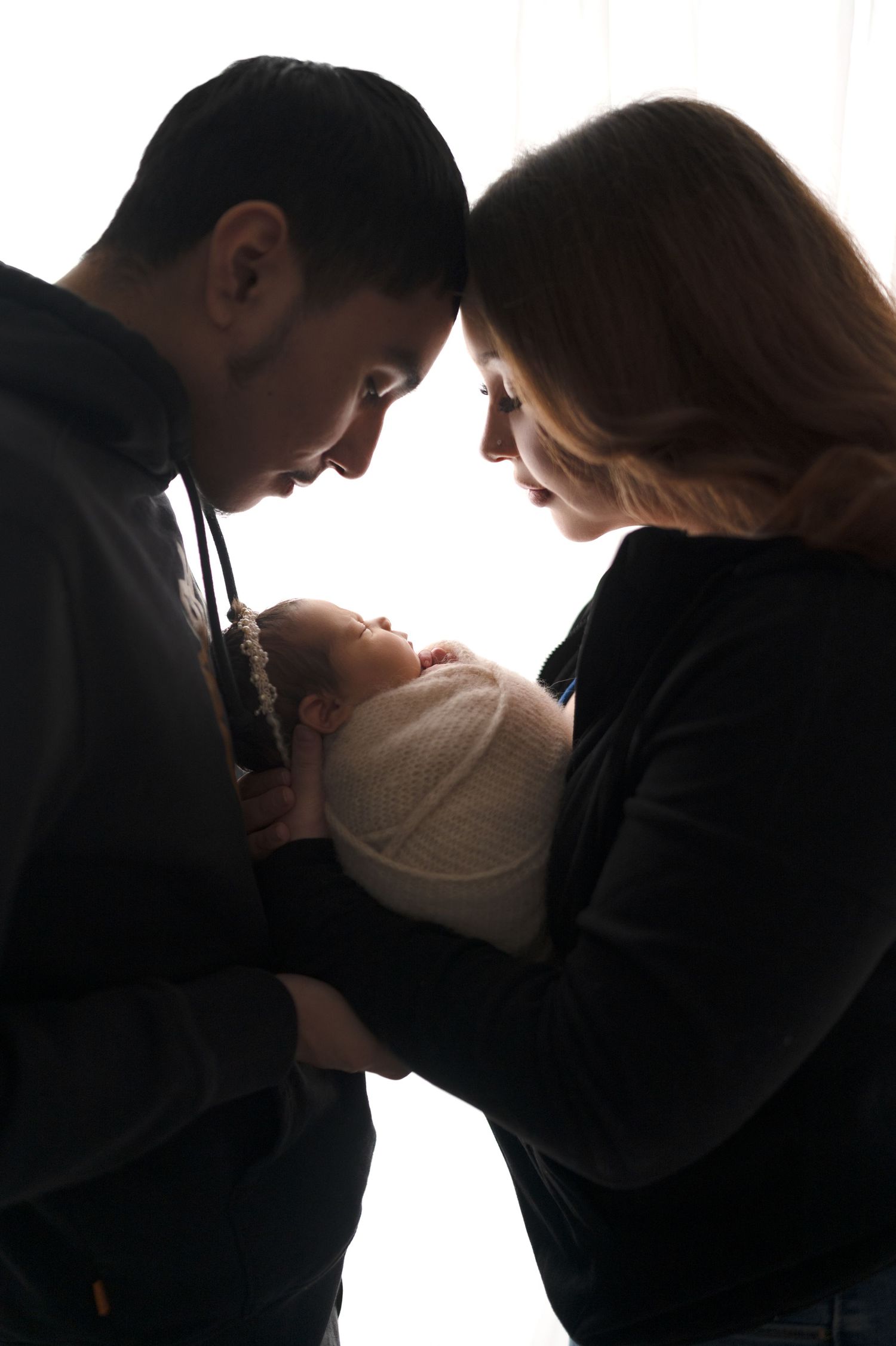 Silhouetted portrait of parents tenderly holding their newborn against white background.