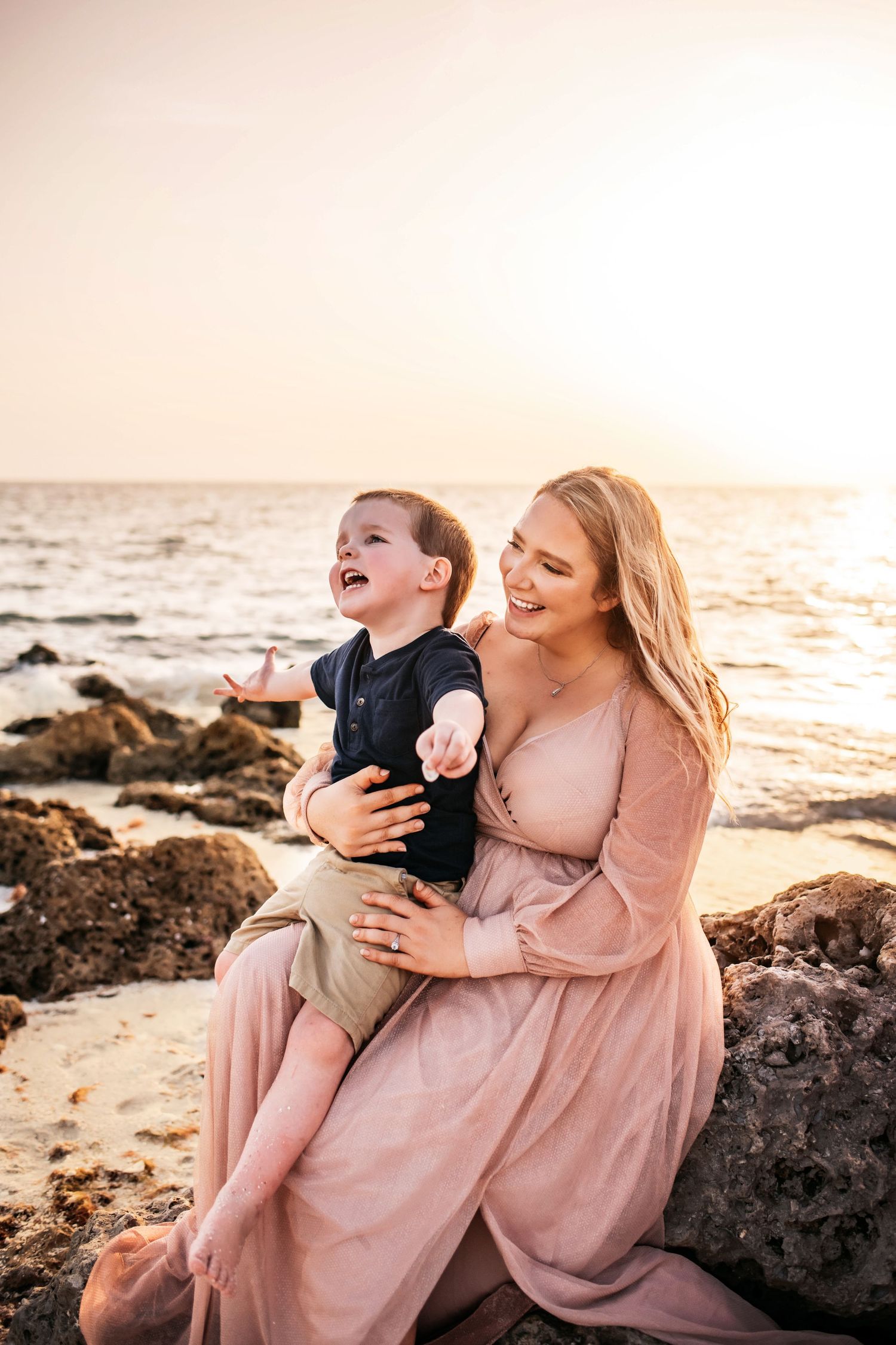 A joyful moment between parent and child laughing together on rocky beach at sunset.