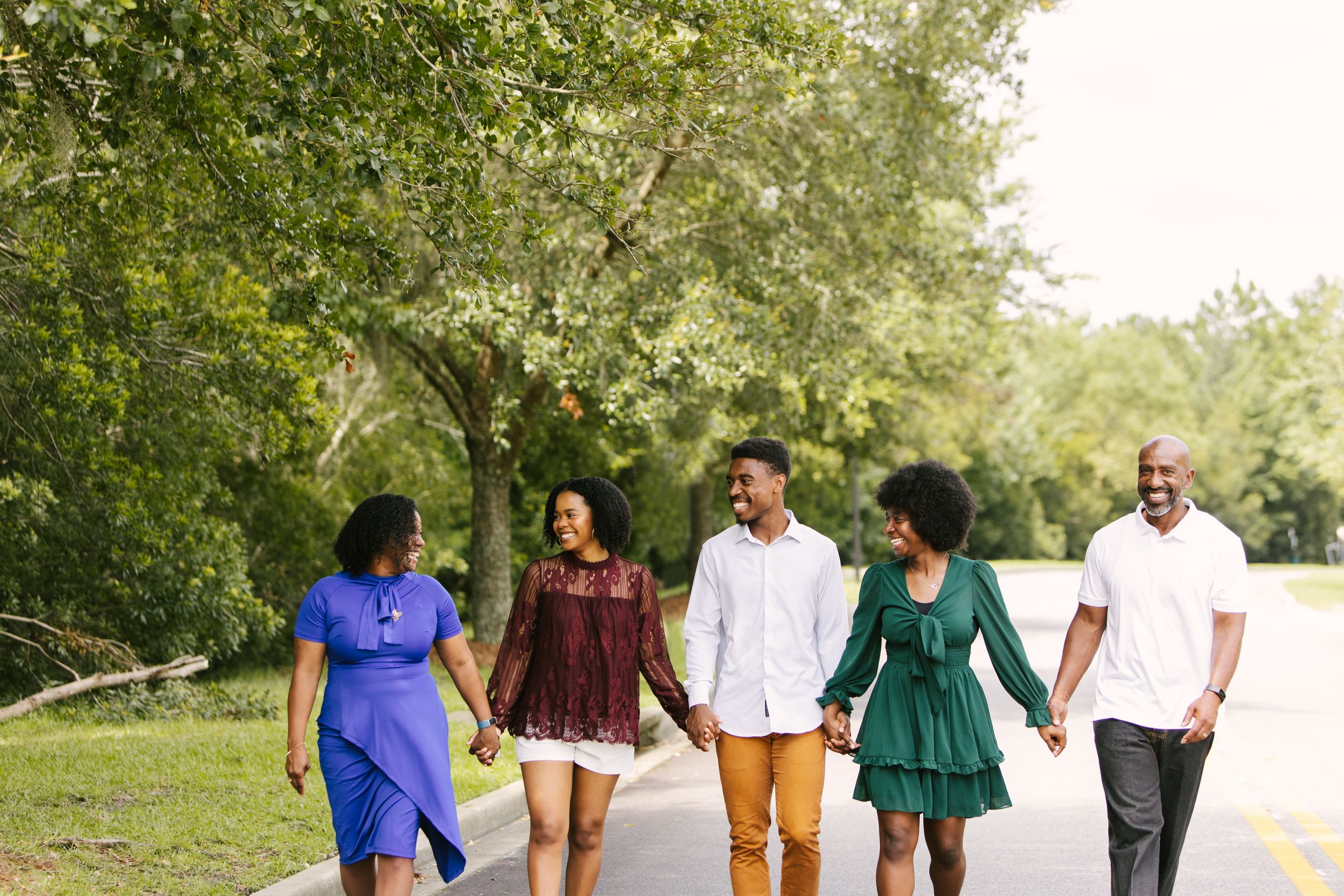 Group of friends walking together and holding hands on path through green park.