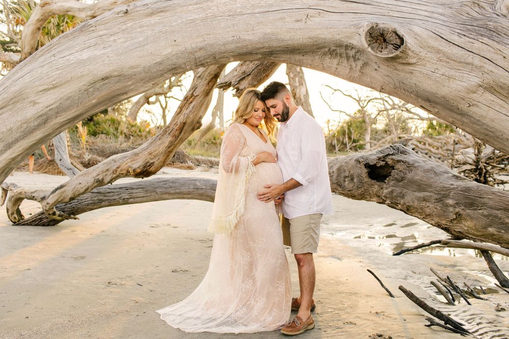 Ethereal beach engagement photo under a natural driftwood arch at sunset.