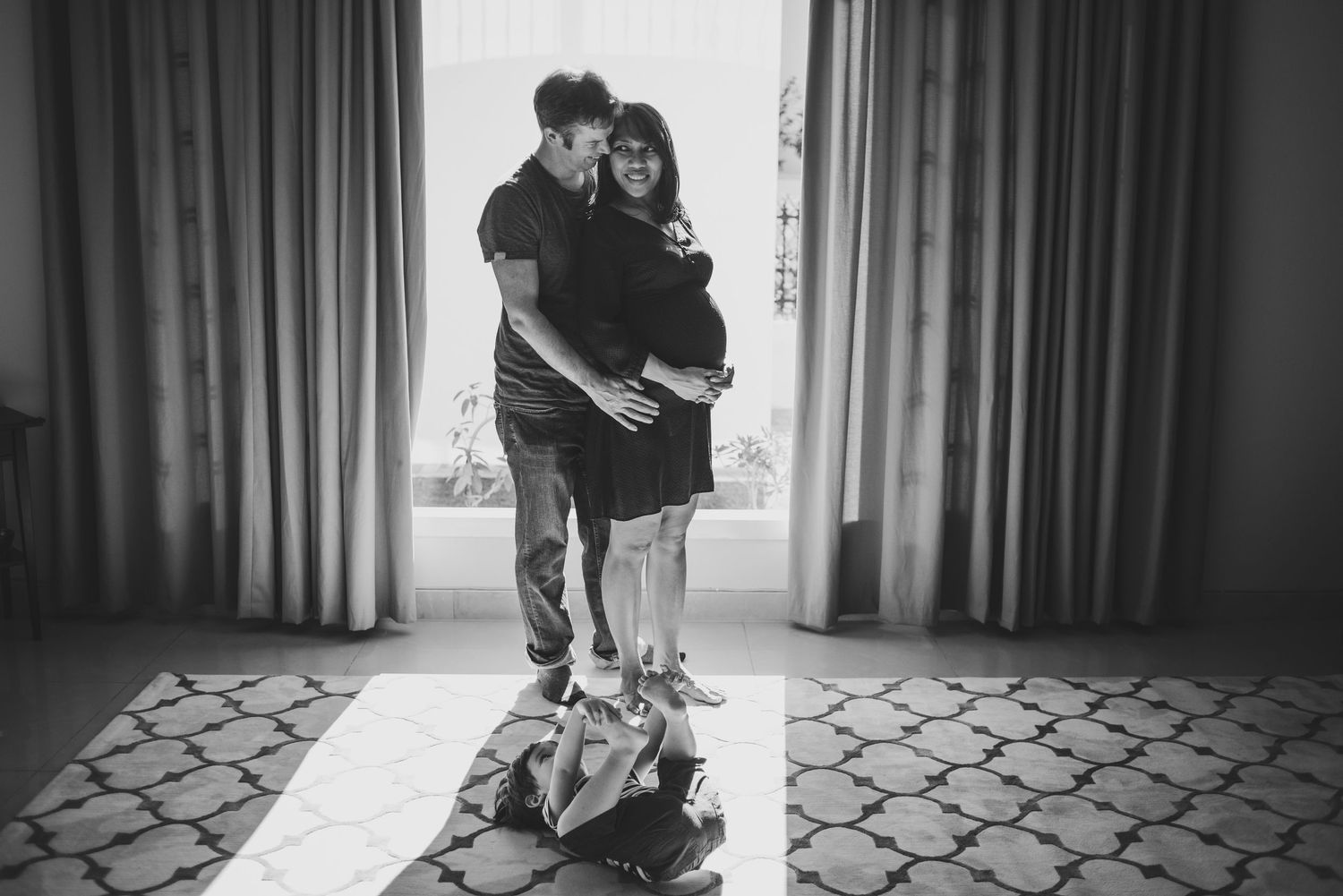 Intimate black and white portrait of couple standing between curtains.