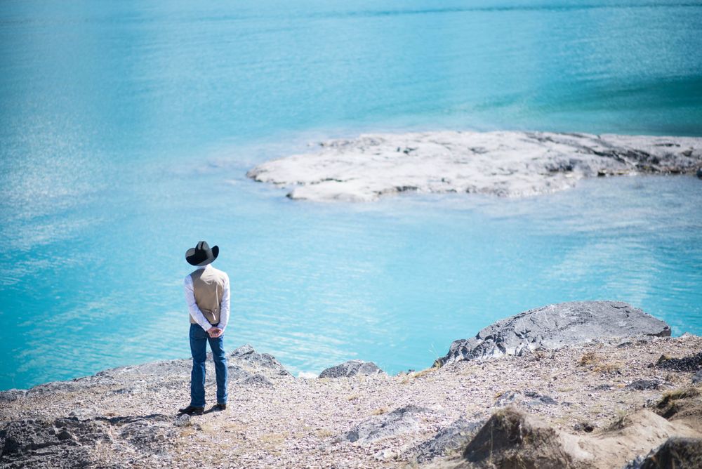 Person standing on rocky outcrop overlooking turquoise mountain lake.