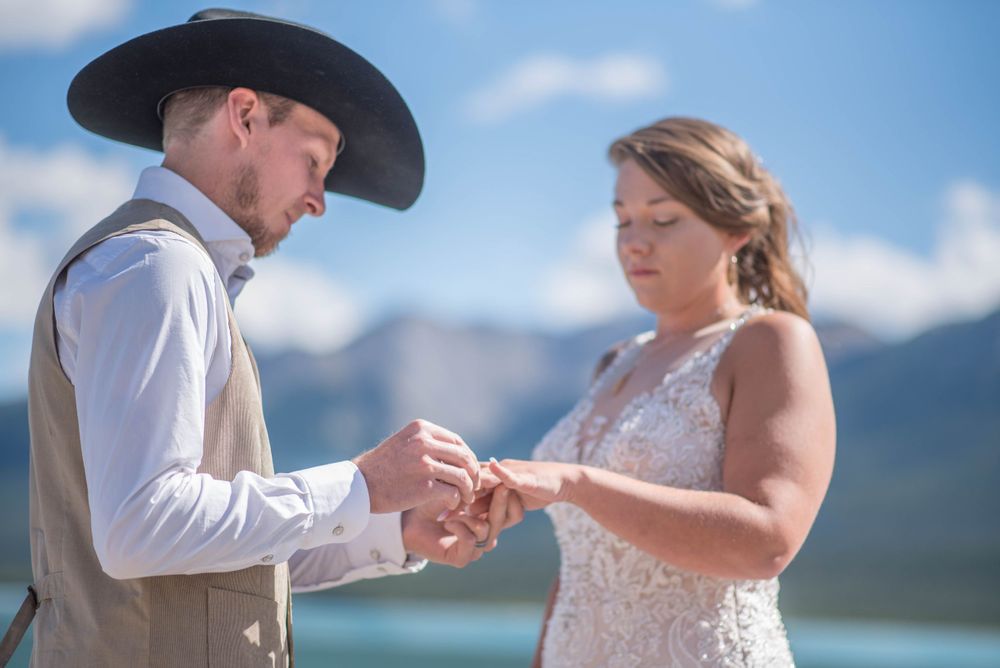 A couple exchanges rings during their wedding ceremony against a mountain backdrop.