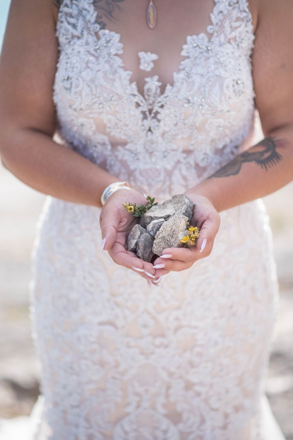 Close-up of bride holding small rocks in her hands while wearing lace wedding dress.