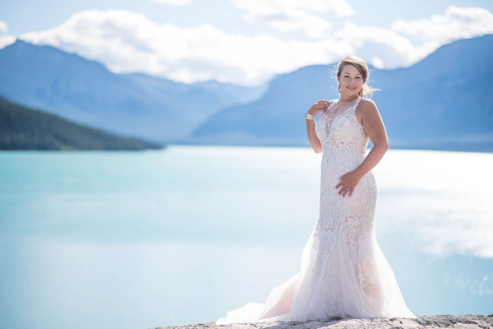 Wedding dress silhouette against turquoise mountain lake and cloudy sky.