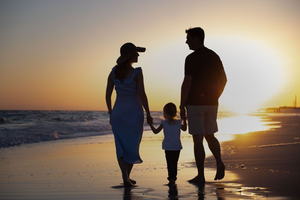 A small, happy family taking a leisurely walk on the beach during a captivating sunset, with the golden hues of the sky