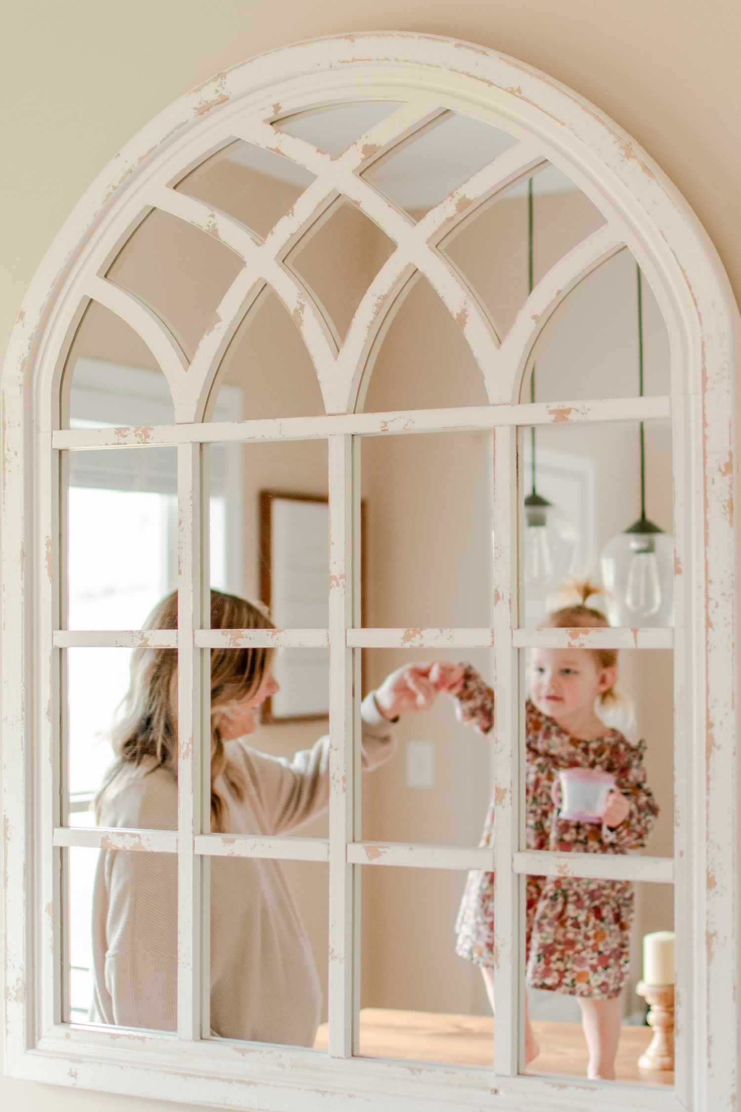 White arched window mirror reflects two figures playing together in a bright interior space.