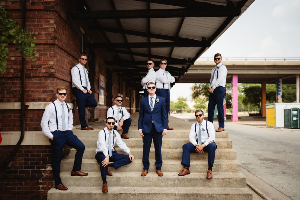 Groomsmen in navy suits and suspenders pose on brick steps for a casual group photo.