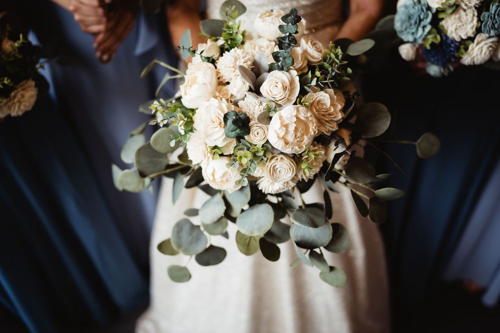 Elegant white and cream bridal bouquet with eucalyptus leaves against blue bridesmaid dress.