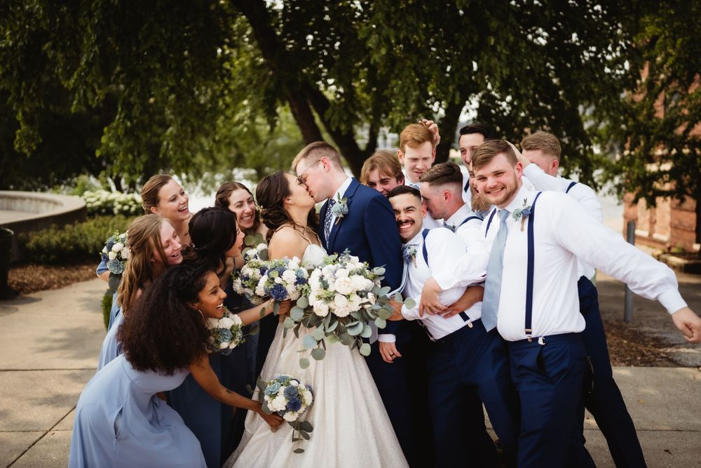 Wedding party laughs together outdoors in navy and white attire with bouquets.