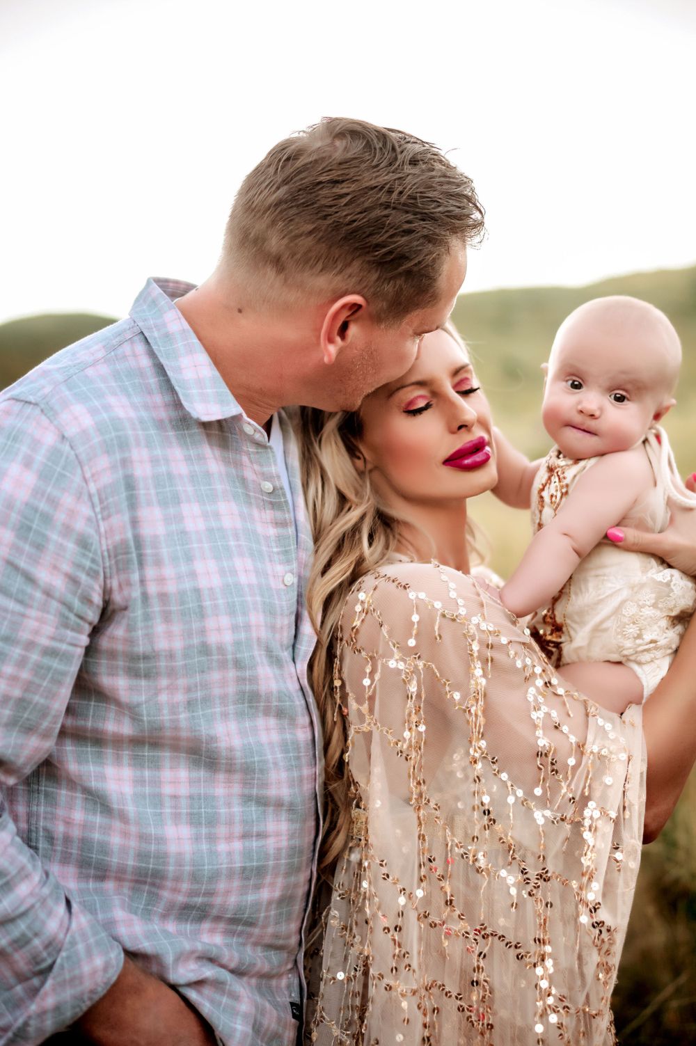 A romantic family photoshoot outdoors featuring a couple in pastel clothing holding a baby against a natural backdrop.