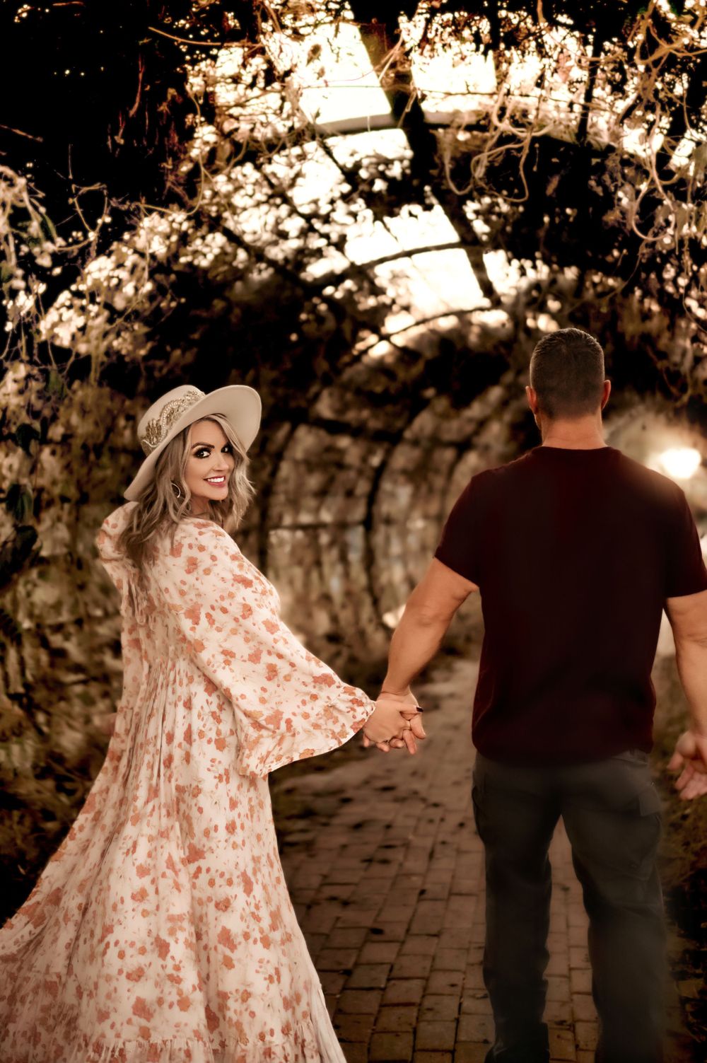 Romantic couple holding hands in tunnel of vines during sunset.