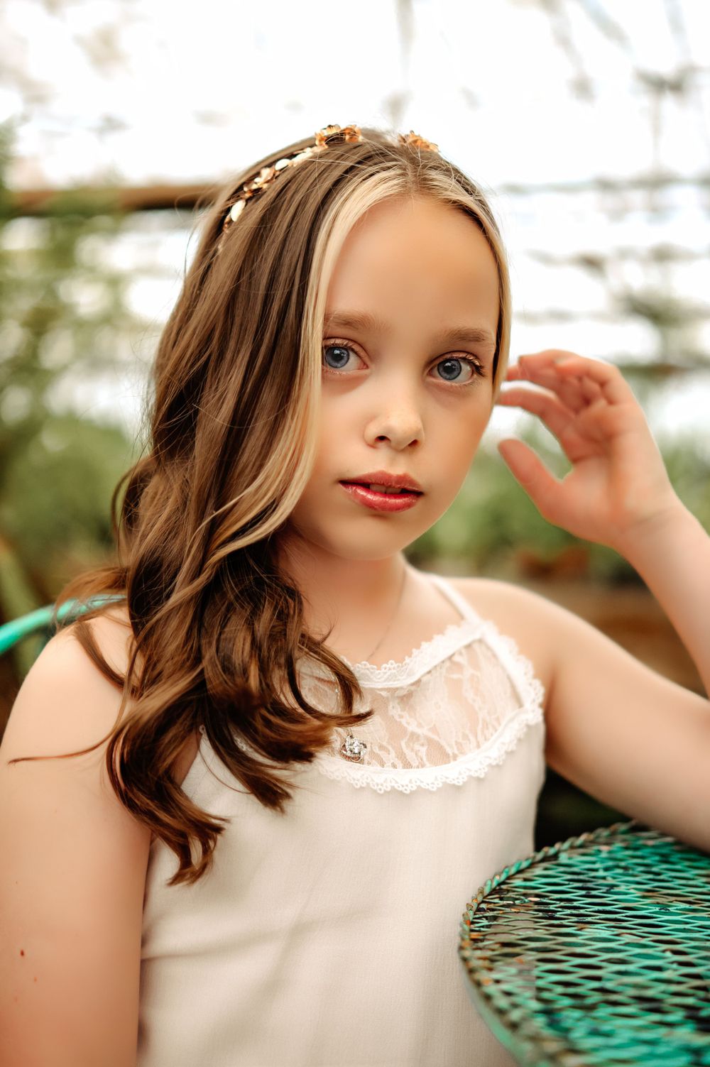 Young person in white lace top poses with delicate hand gesture.
