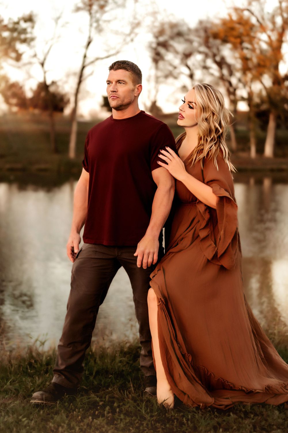 Couple in formal wear posing dramatically by lake at sunset.
