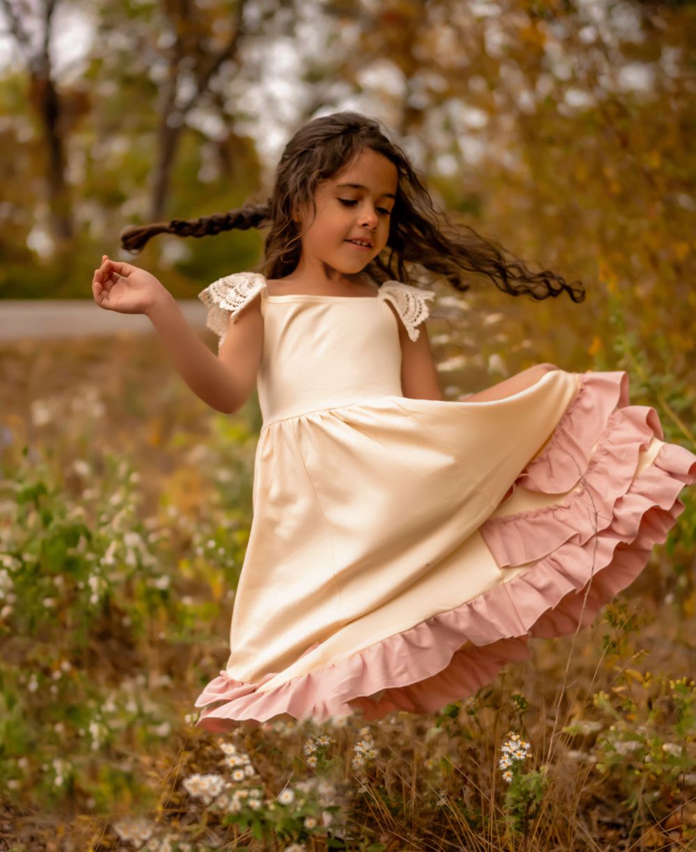 Young dancer twirling in cream dress with pink ruffles among autumn foliage.