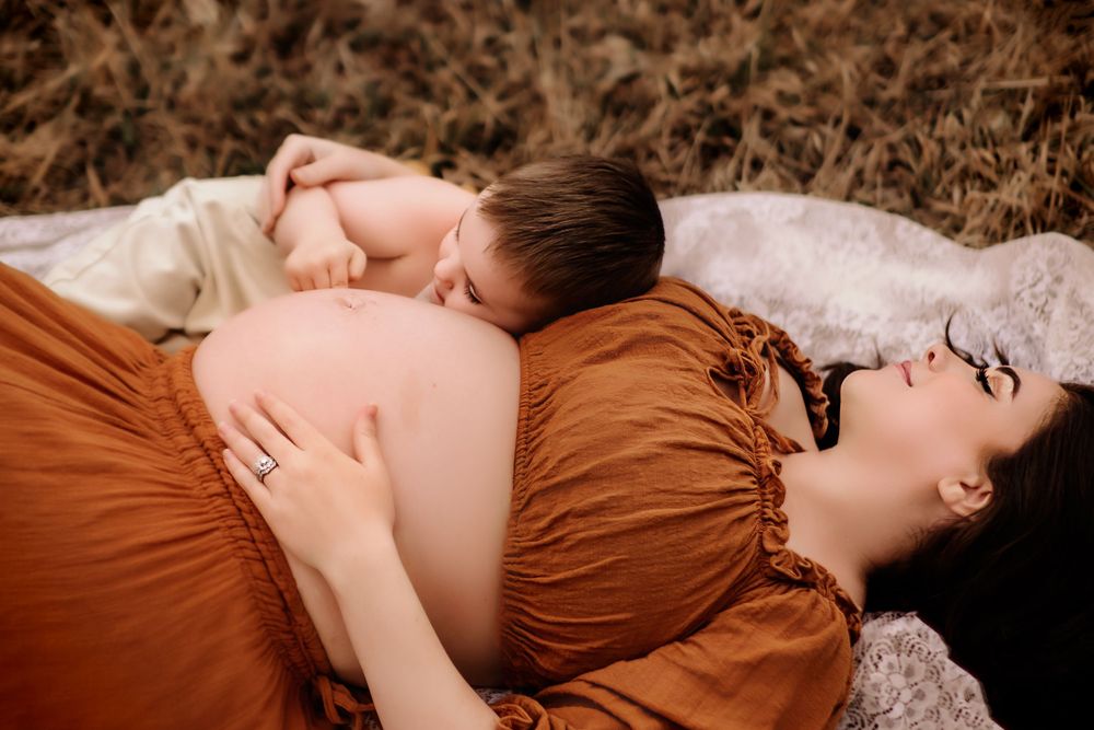 An intimate maternity photo of a couple lying down in earth-toned clothing outdoors.