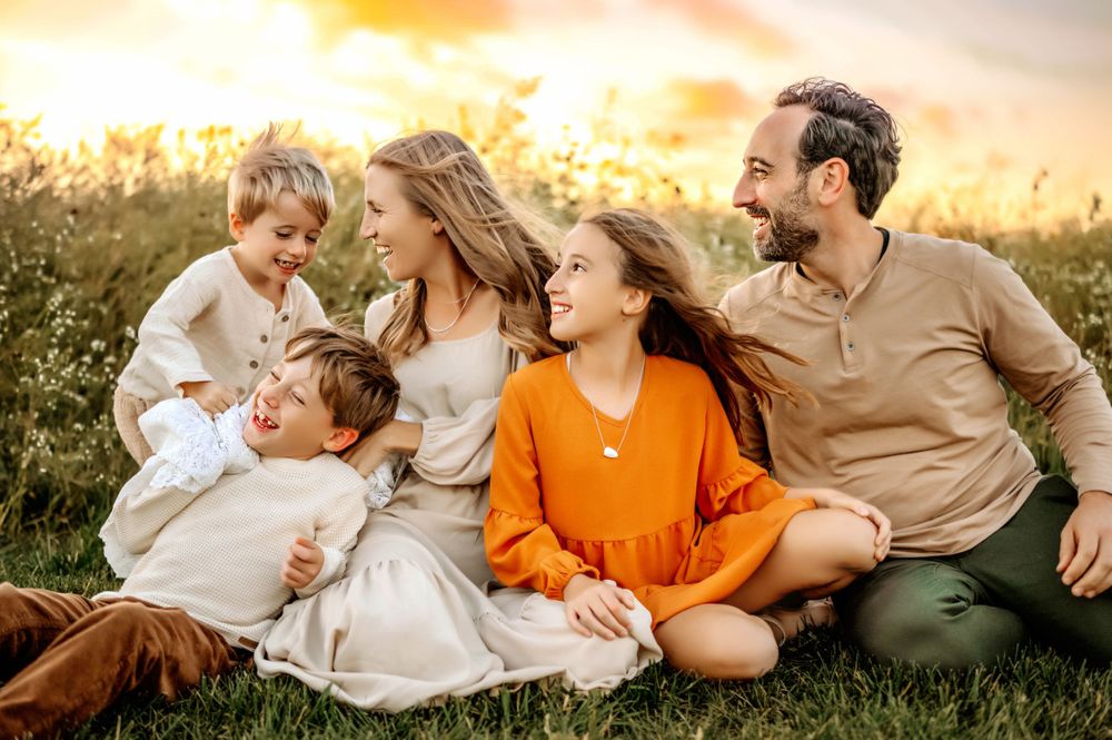Family sitting together in field during golden hour sunset.