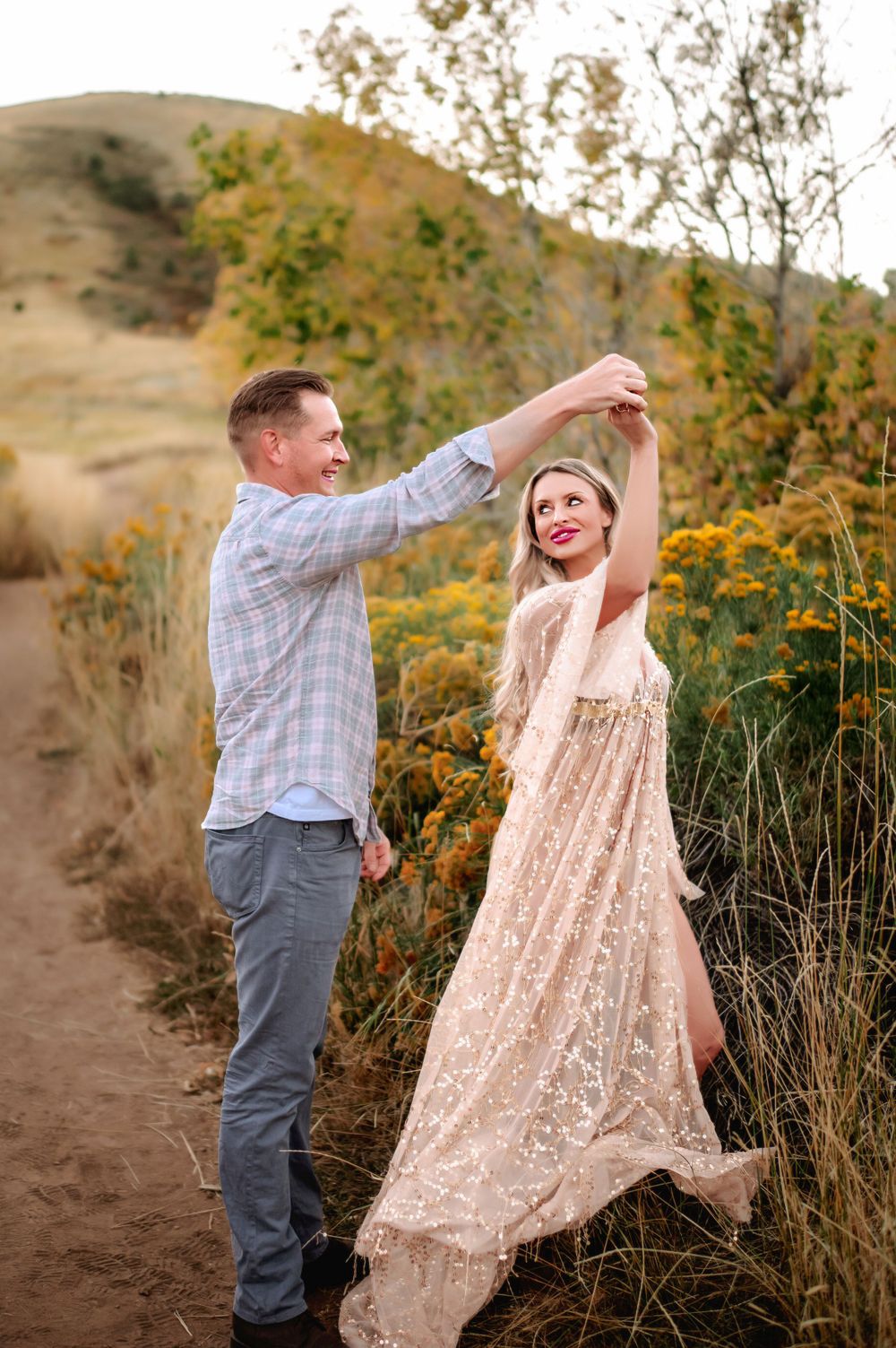 A couple dancing together on a dirt path surrounded by golden wildflowers and rolling hills.