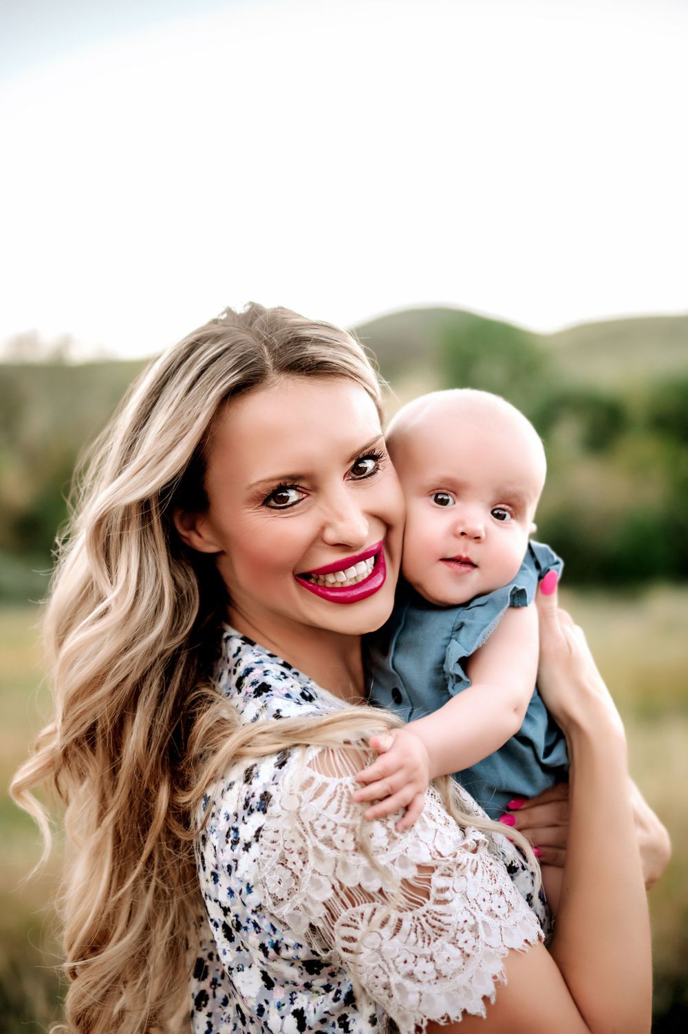 A joyful portrait in nature featuring a blonde woman in lace holding a small baby.