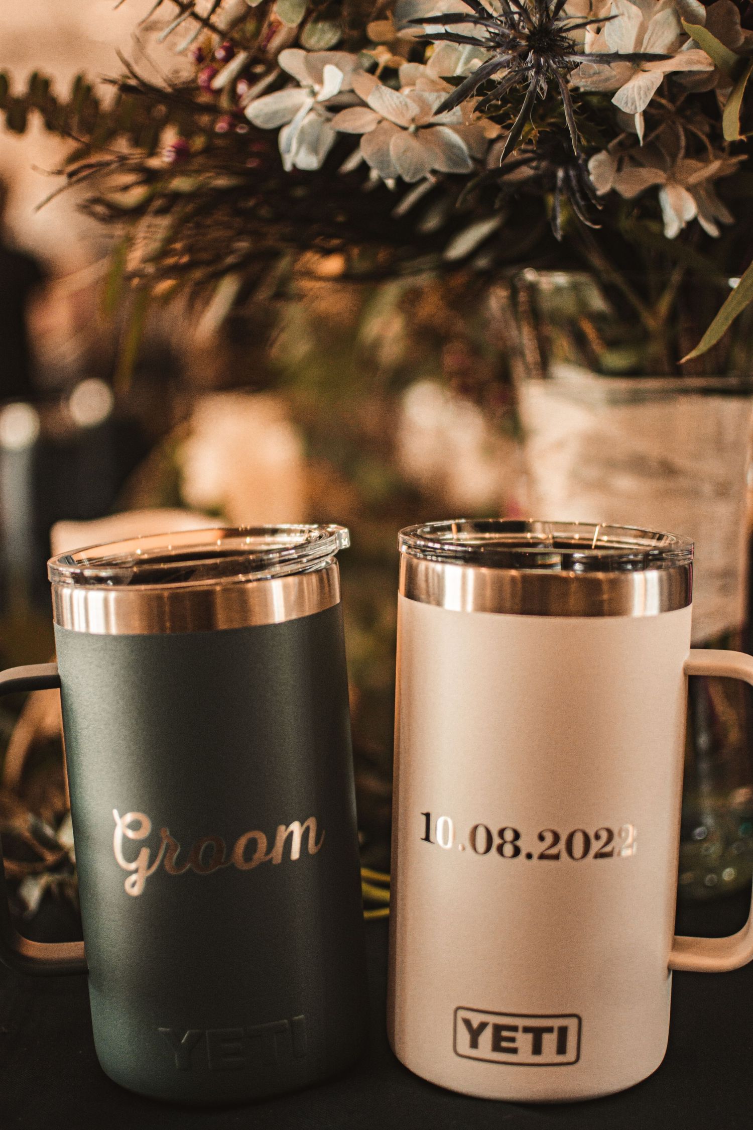 Custom Yeti tumblers for groom and wedding date displayed with floral decorations.