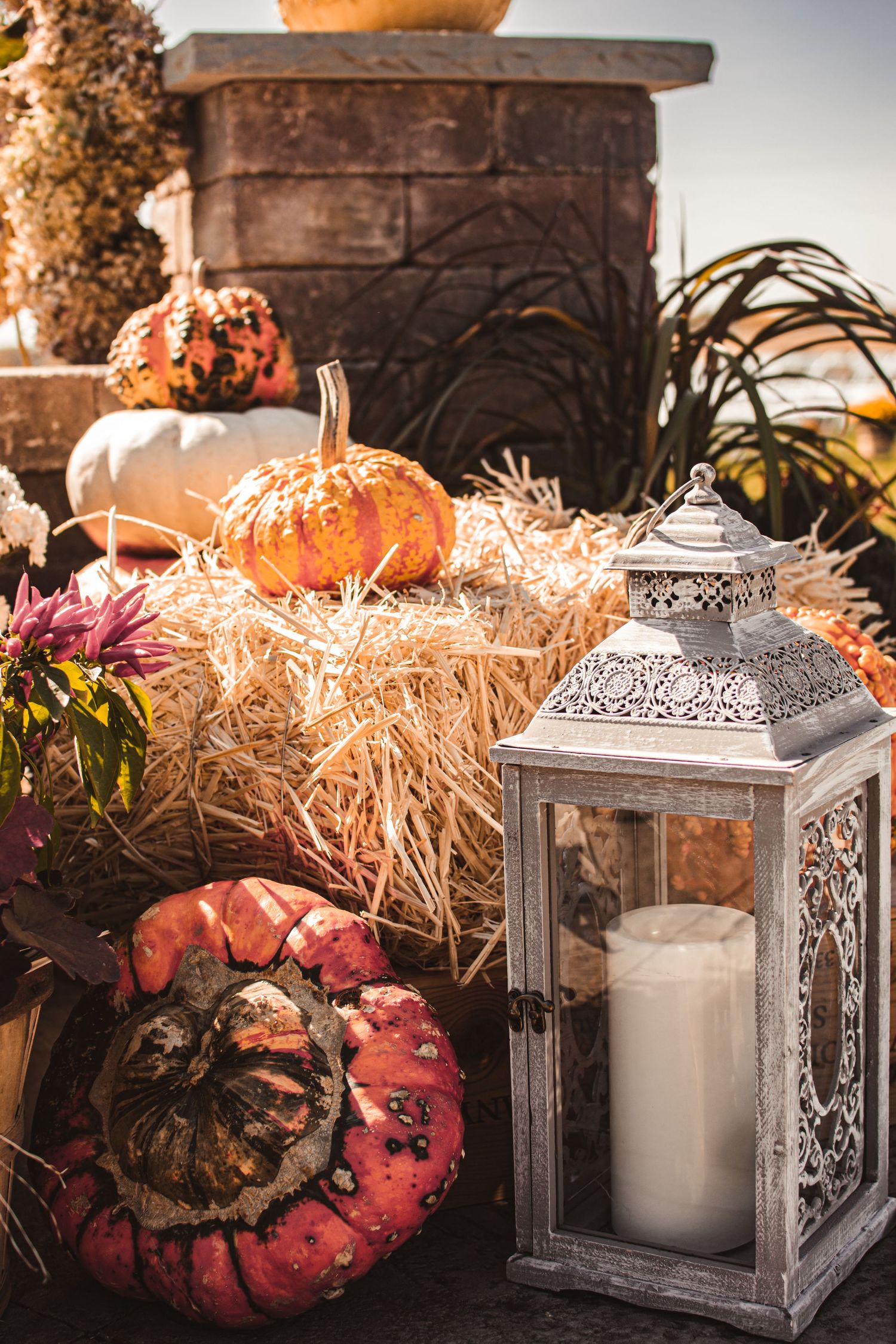 Fall wedding decor with vintage lantern, pumpkins and hay bales creating cozy autumn atmosphere.