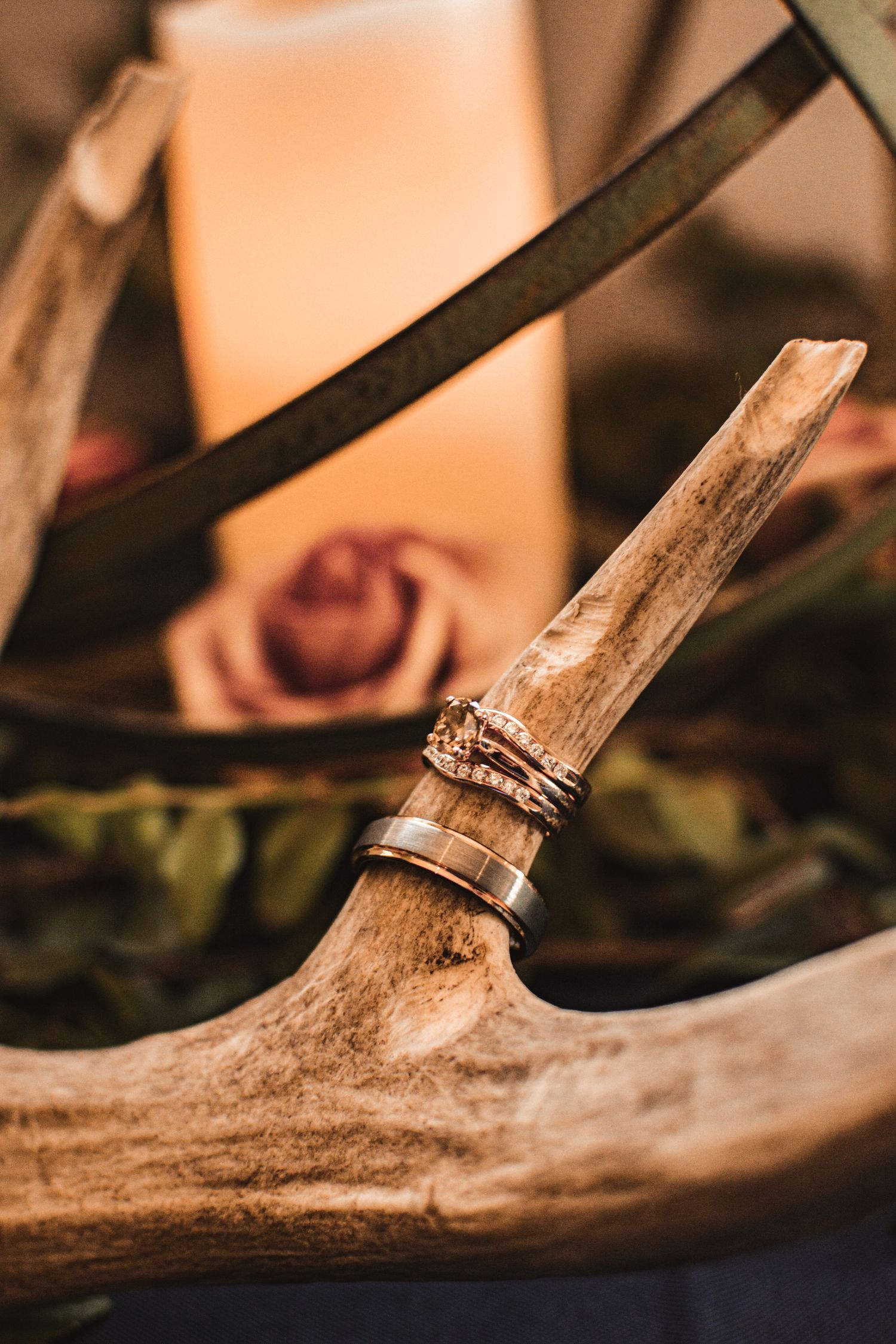 Wedding rings displayed on antler decor with metal sphere and candle in rustic setting.