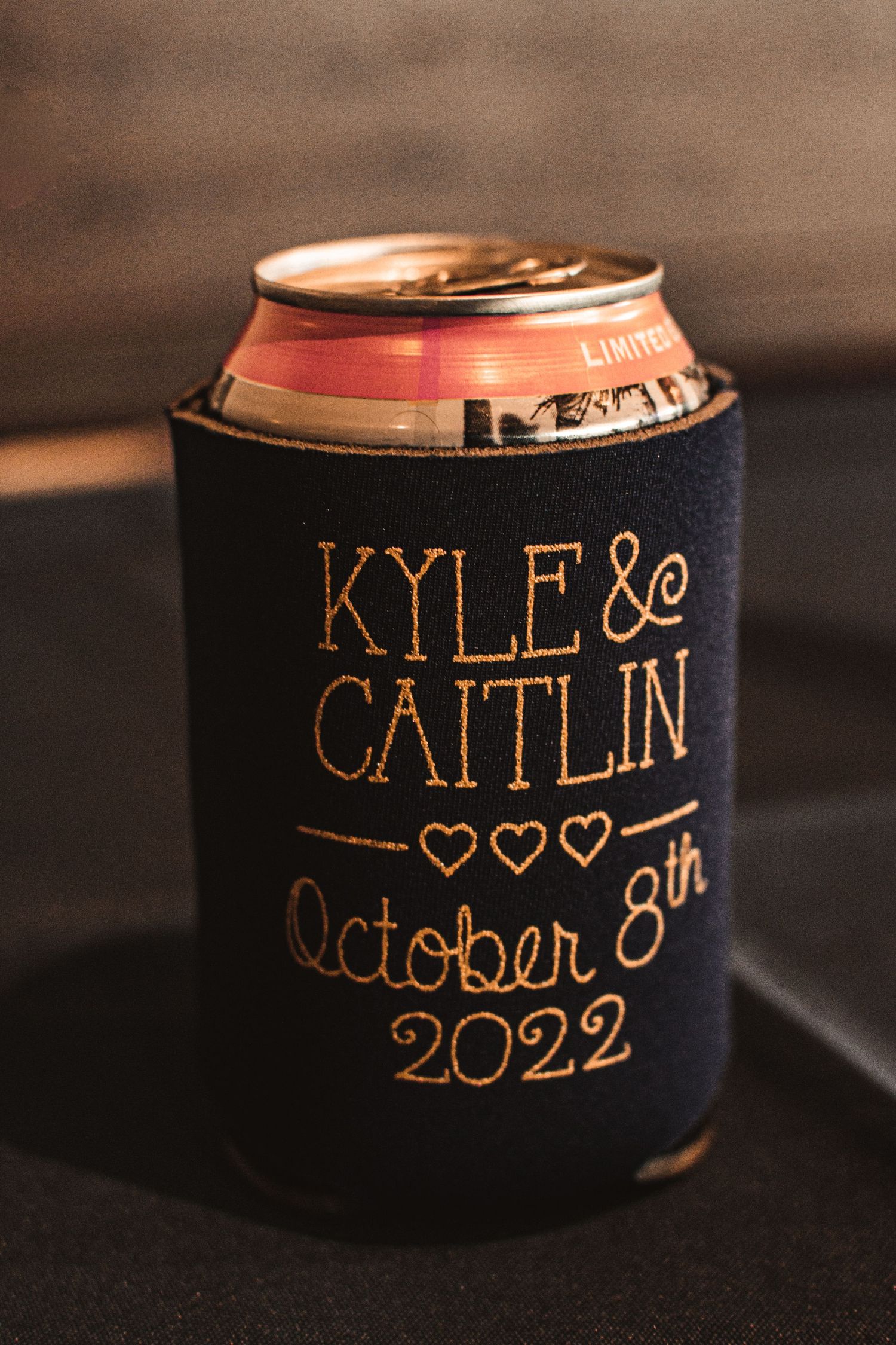 A custom wedding koozie displaying names and date 'Kyle & Caitlin October 8th 2022' in gold lettering.
