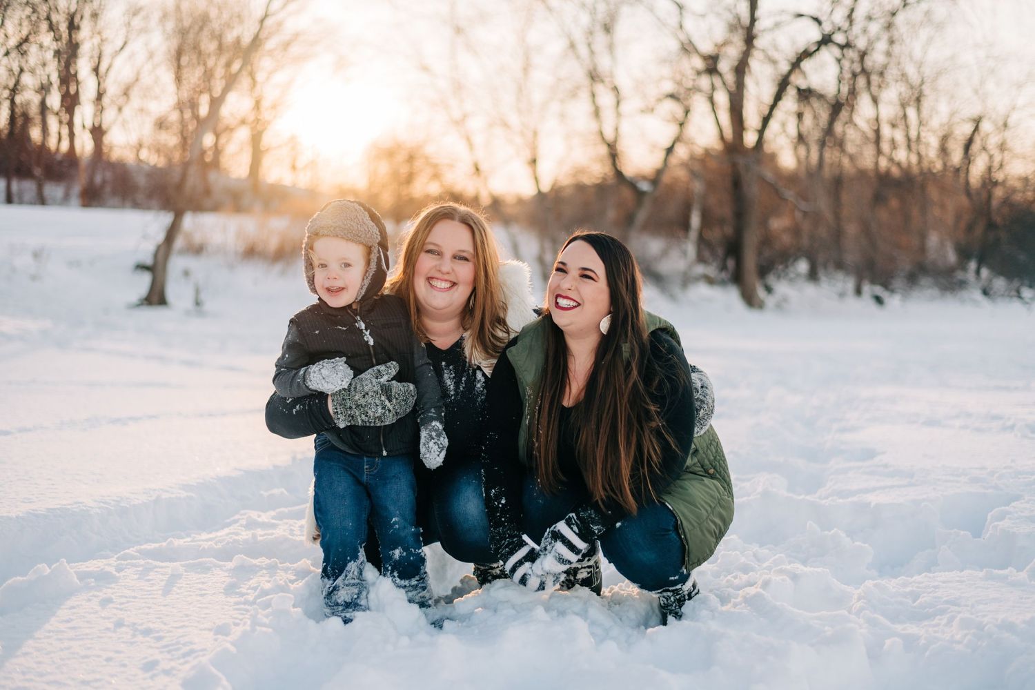 photo of two women snuggling their nephew on a snowy beach at sunset
