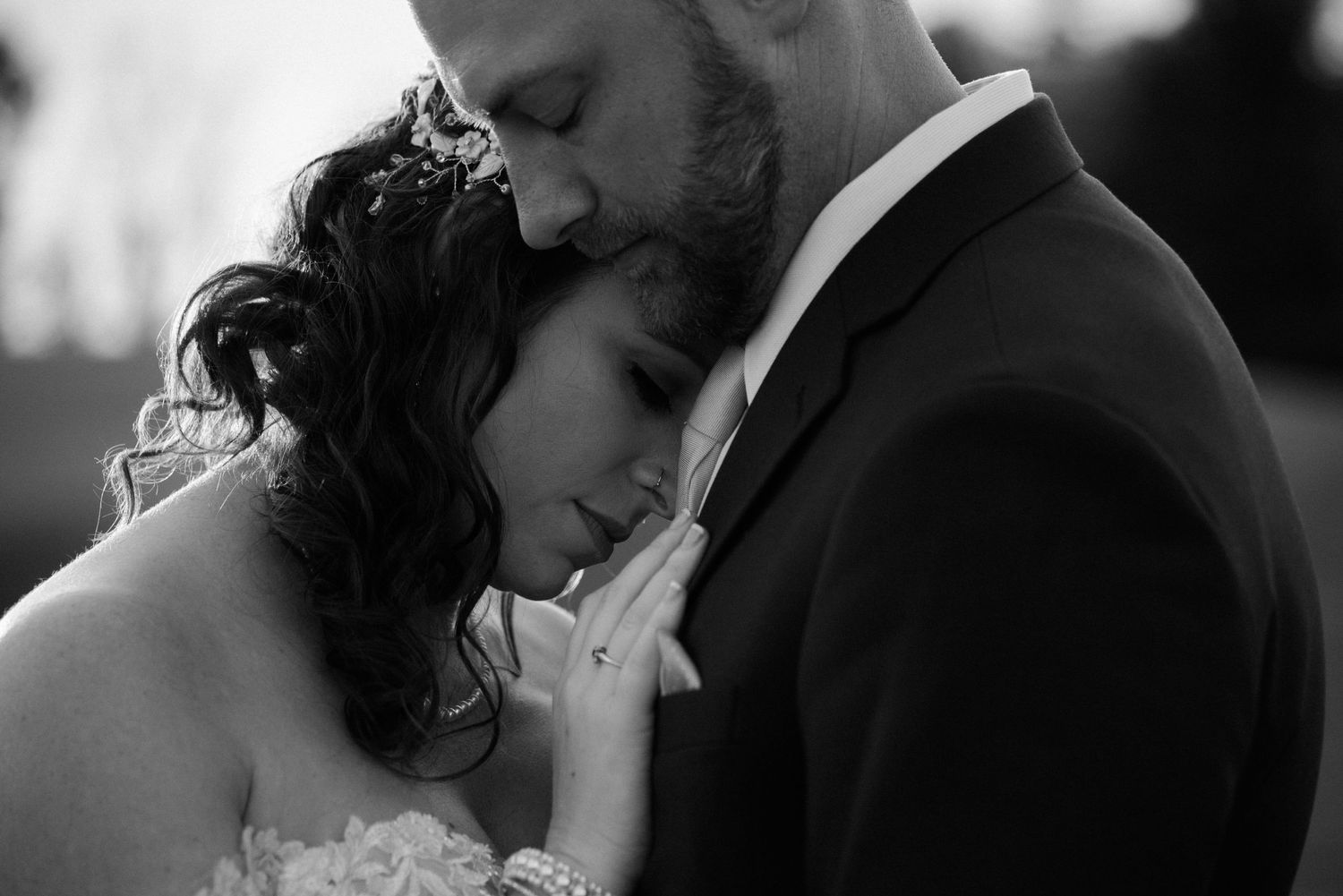 An intimate black and white moment between a couple in wedding attire showing tender affection.