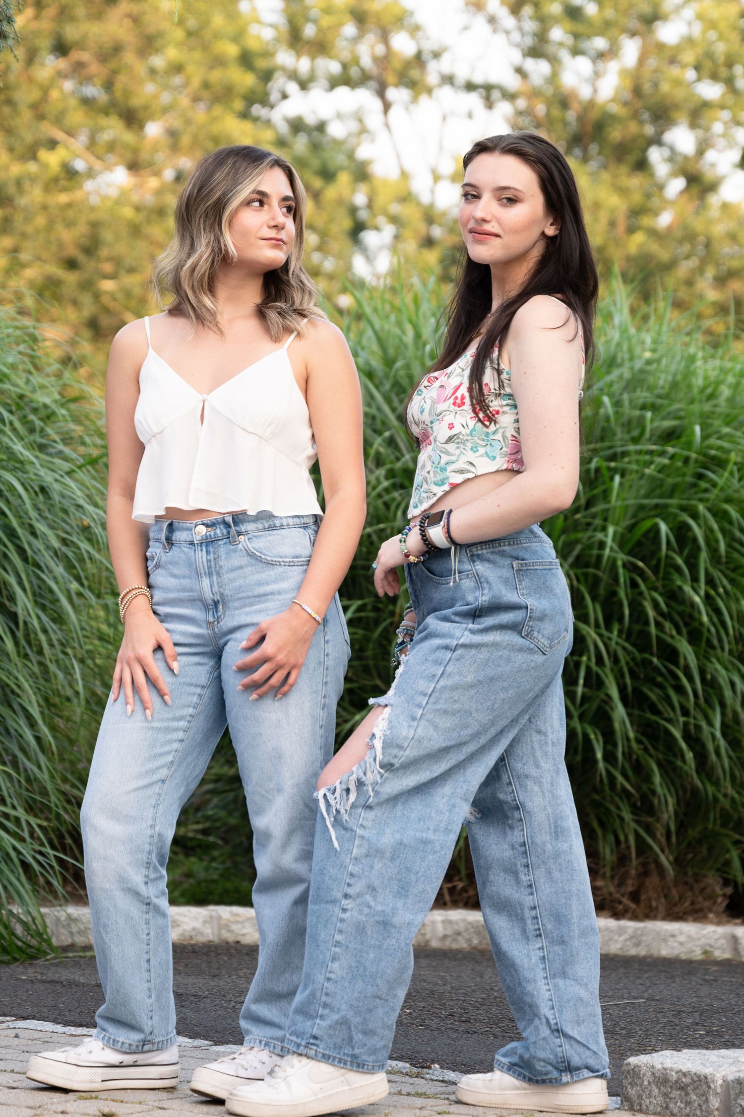 Two friends in casual denim and white tops pose together outdoors.