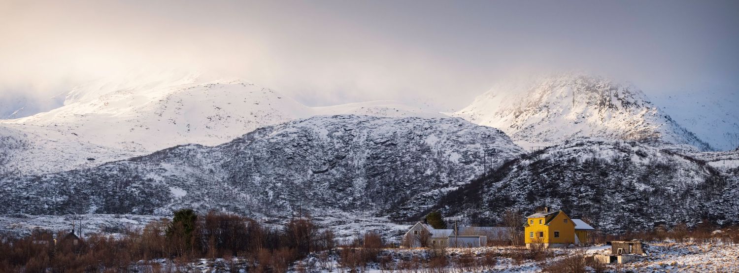 Snow-capped mountain peaks rise dramatically against a cloudy sky in a panoramic winter landscape.