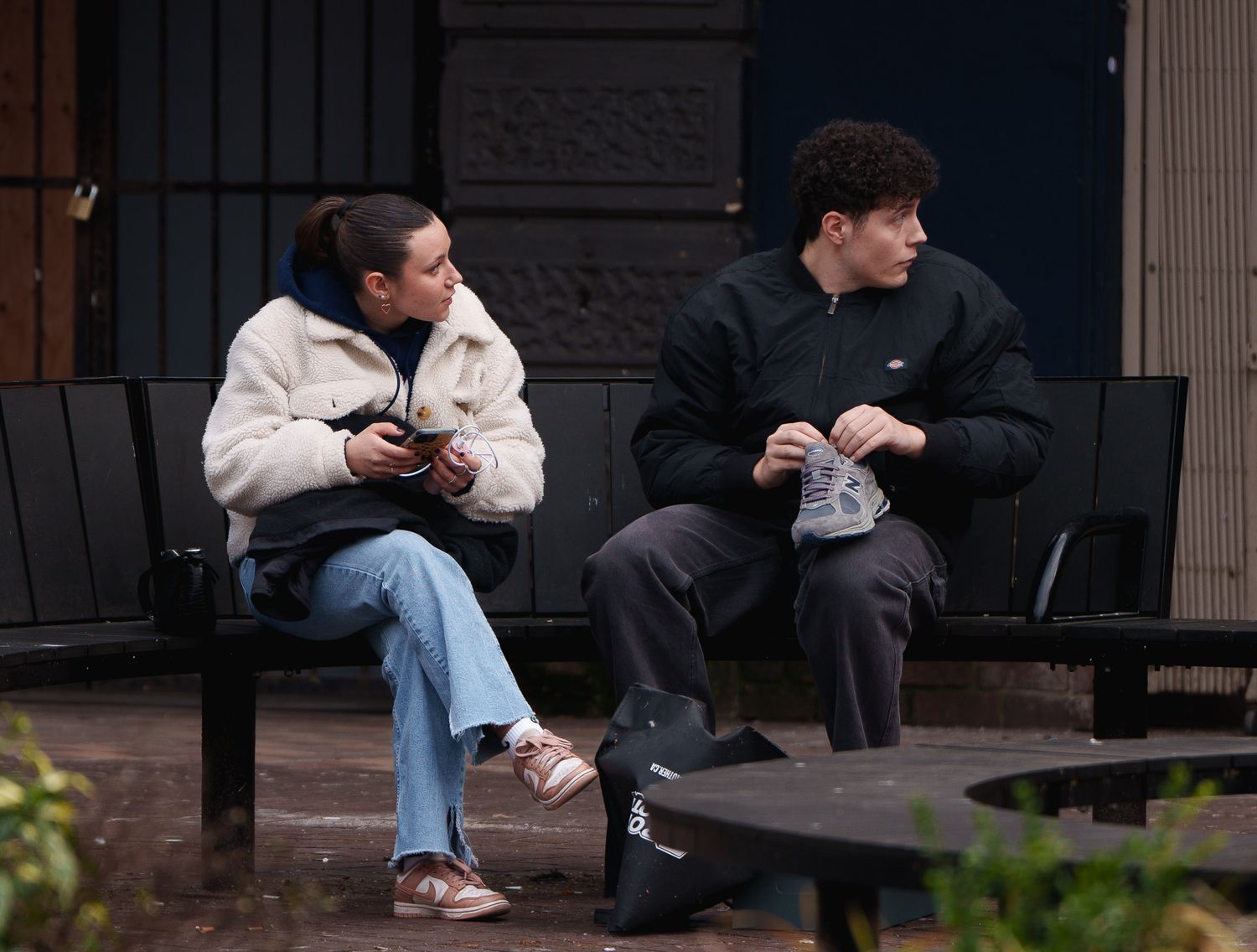 A woman holding her phone and a man with a shoe on his lap looking at their left, street photography