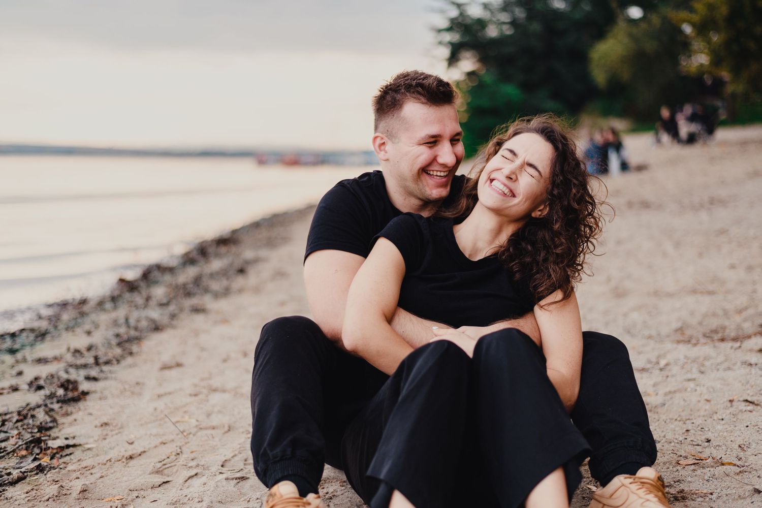 Couple in black clothing sitting together on a beach at sunset.