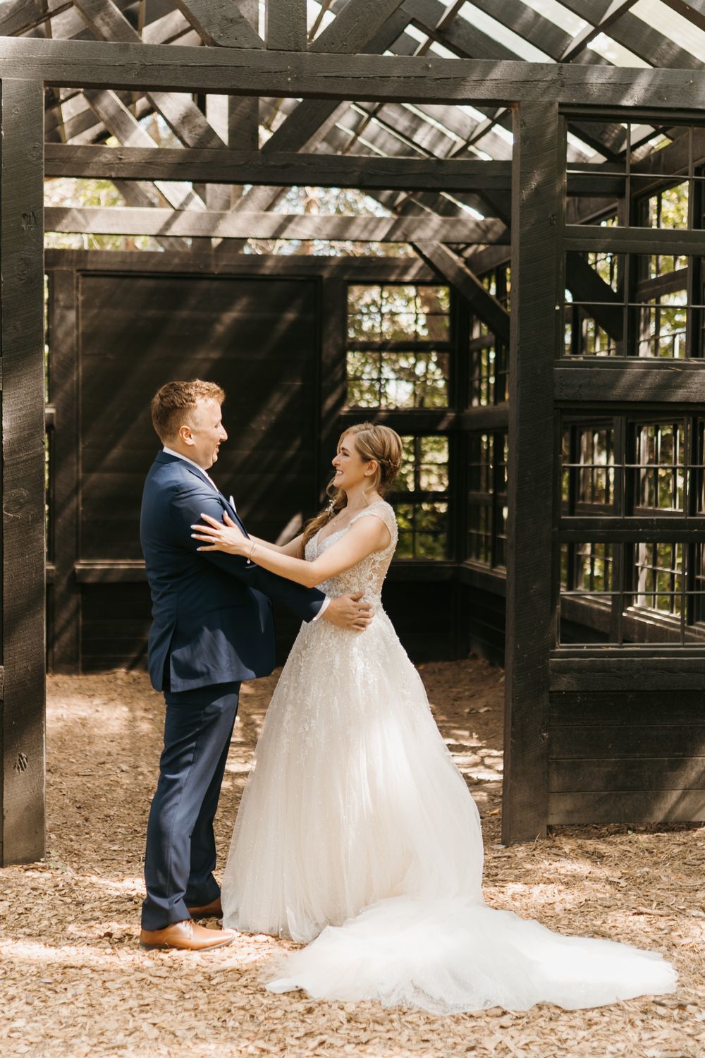 Bride and groom share a joyful first look moment inside a rustic dark wooden greenhouse wedding venue.