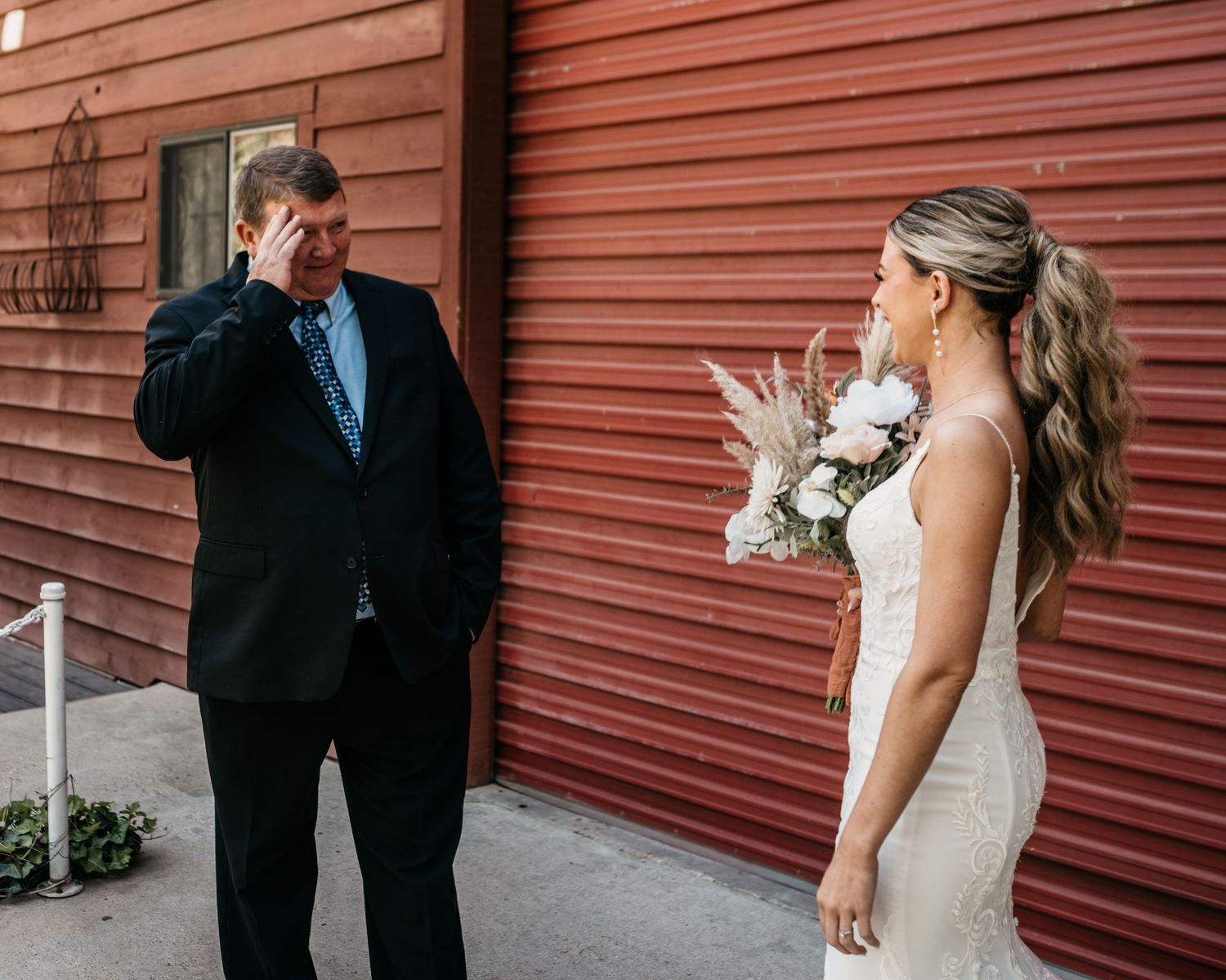 Emotional first look reaction between bride and groom against red barn backdrop.