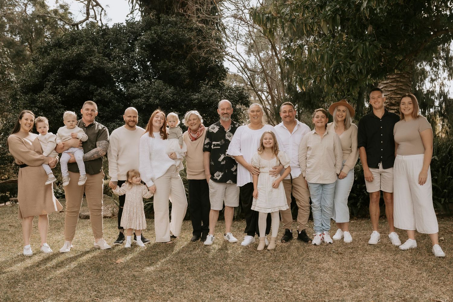 Large extended family in coordinated white and neutral outfits posing outdoors.