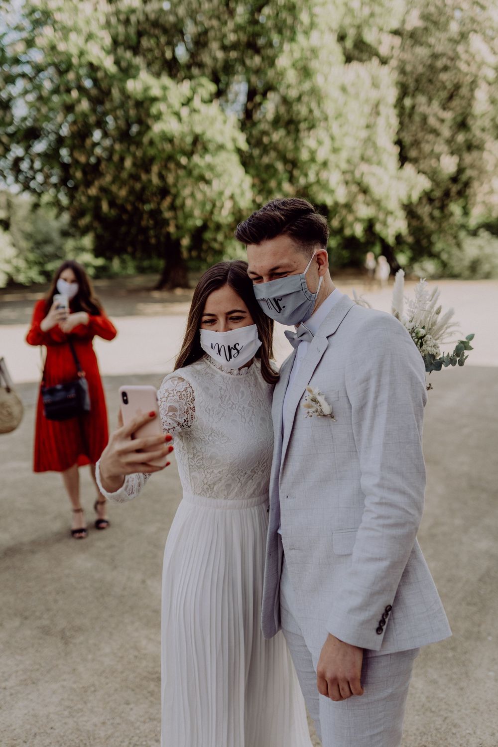 A couple in wedding attire taking a selfie while wearing protective face masks.