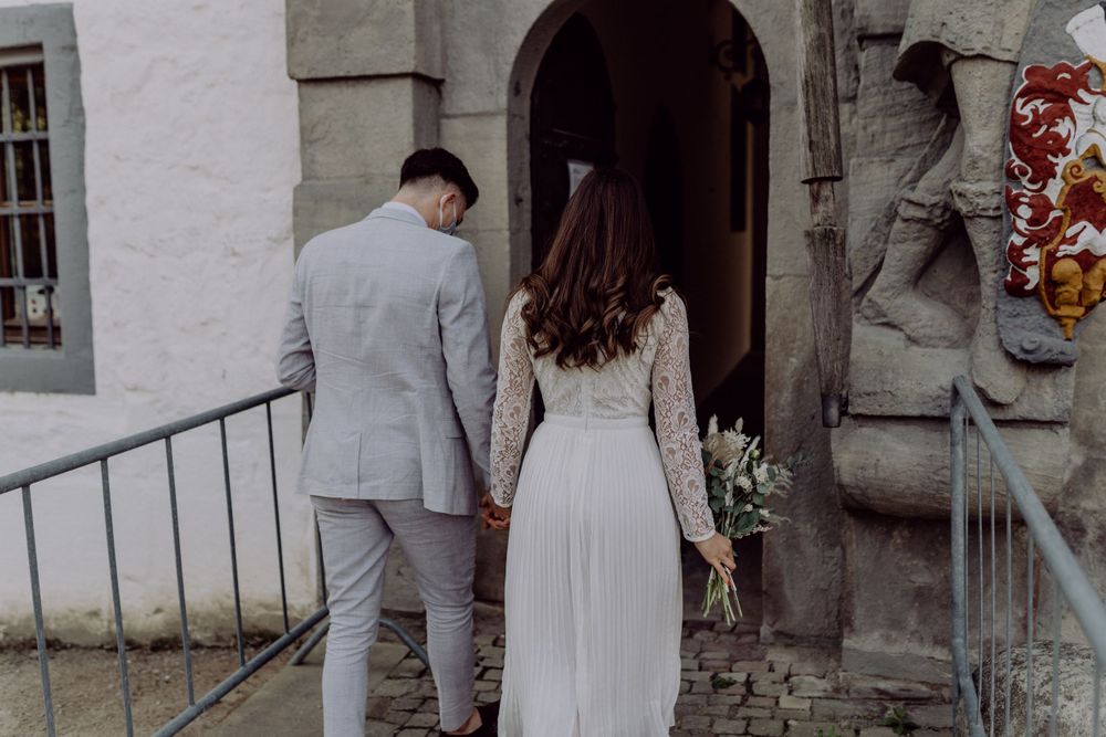 A couple in formal attire walking up stone steps toward an arched entrance.