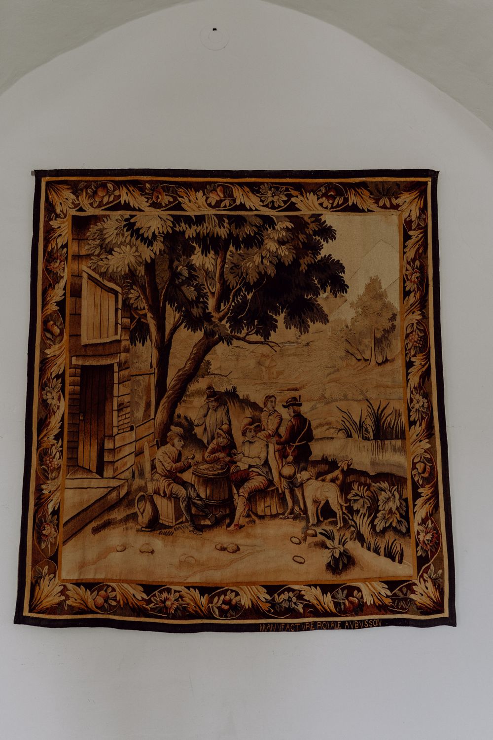 Vintage tapestry depicting a rustic countryside scene with figures and animals outside a building.