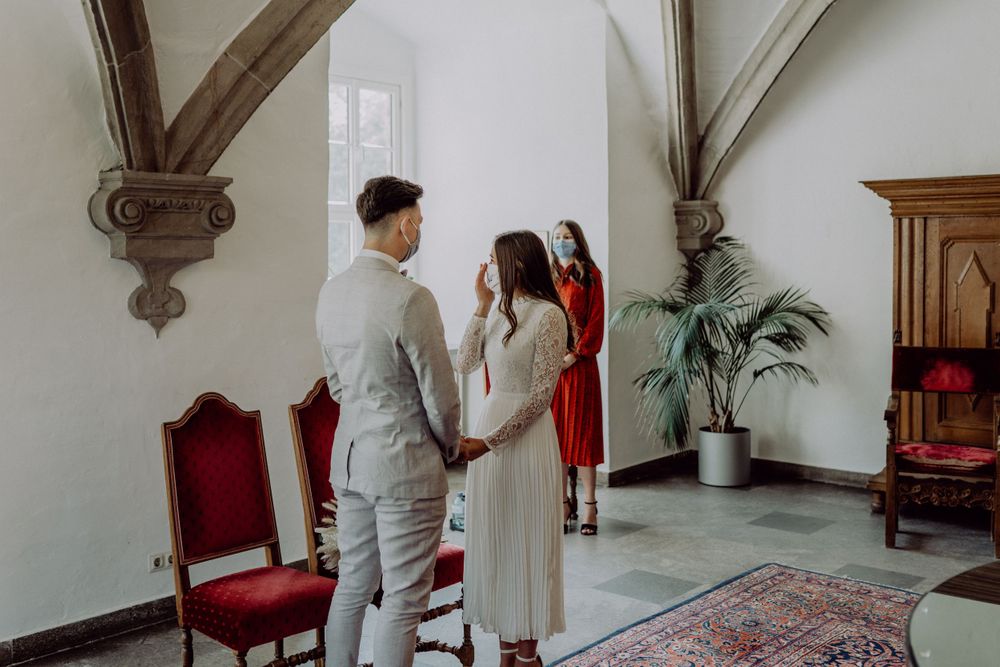 Wedding ceremony in bright room with gothic architectural details and red velvet chairs.