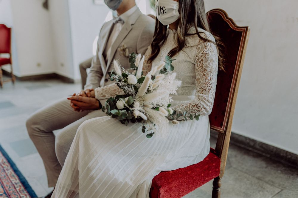A couple sits on red velvet chairs during an intimate wedding ceremony.