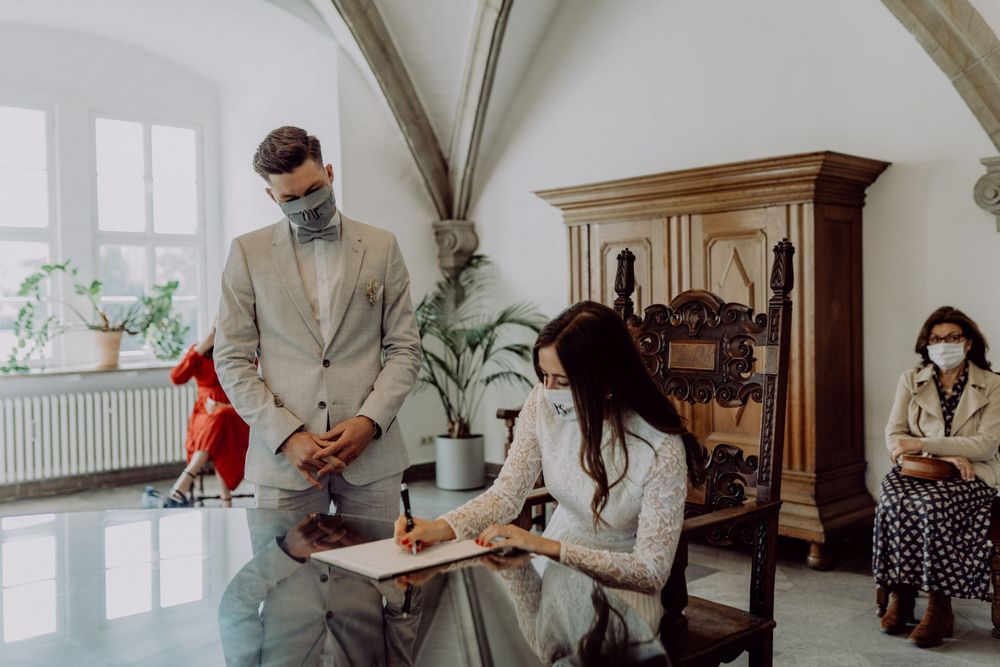 Two people sign documents during a ceremony while another person in red watches from a distance.