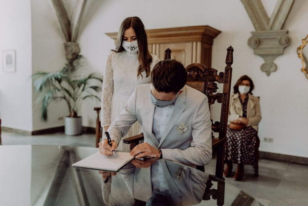 Two people sign official documents at a ceremony while seated in an elegant room with arched ceilings.