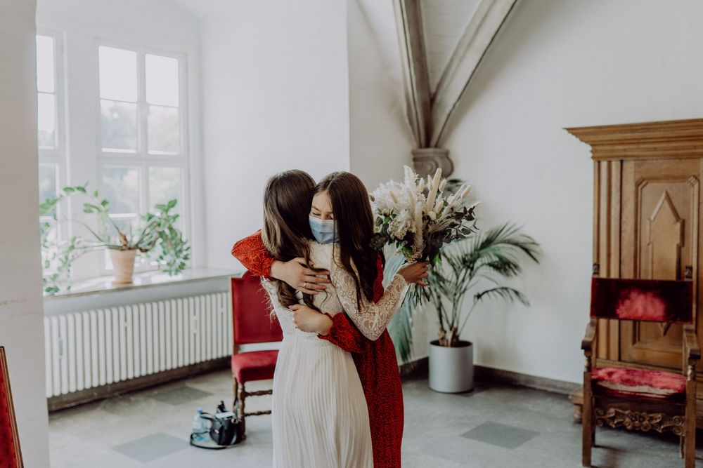 Two people embrace in an elegant room with arched windows and indoor plants.
